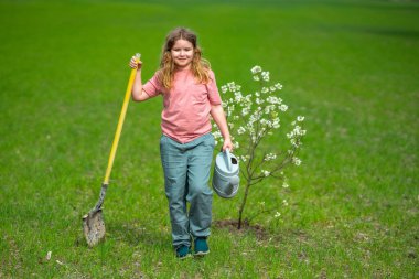 Şirin bir çiçek ve bahçedeki sulama ağacı. Bitkilerin bahar etkinliği. Çocuk kürek ve su bidonuyla çalışıyor. Çocuk meyve ağacı dikmiş. Bahçıvan çocuklar. Çocuk yetiştirme bitkisi ve ağaç bakımı