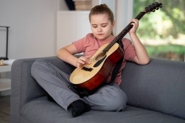 Gitar çalan çocuk. Çocuk oturma odasında gitar çalma alıştırması yapıyor. Çocuk içeride gitar öğreniyor. Müzik dersi sırasında gitarlı bir çocuk. Akustik gitar çalan bir çocuk. Çocuk şarkıları çalışıyor