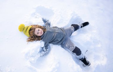 Mutlu çocuk kışın bir kar meleği yapıyor. Dışarıda karda oynayan bir çocuk. Melek çocuk kışın oynar. Kar melekleri yapan mutlu bir çocukla kış eğlencesi