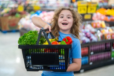 Marketteki çocuk. Sebze dolu alışveriş arabası olan çocuk. Çocuk sebzeleri markette seçiyor. Çocuk bakkaldan alışveriş yapıyor. Çocuklar için market eğlencesi. Meyve pazarındaki çocuk