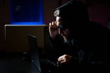 Siber saldırı sırasında bir gece ofisindeki bilgisayar korsanı. Hacker şifreli para çaldı. Dijital para korsanı. Siber saldırı. Ofiste laptop kullanan kapüşonlu bir bilgisayar korsanı.