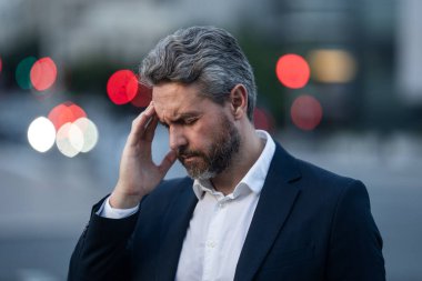 Dışarıda baş ağrısı çeken yorgun bir iş adamı. Takım elbiseli bir adam ağrıyı dindiriyor, migren. İş sorunları. İflas, mali sorun ve kriz konsepti. Milenyum adamı baş ağrısı çekiyor. Migren..