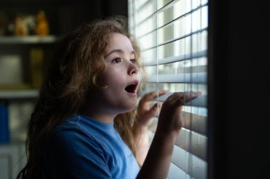 Çocuk evde bekliyor. Evde, pencerenin yanında bekleyen süpriz ergen çocuk. Bekleyen ve pencereden dışarı bakan süpriz çocuk. Şaşırmış çocuk içeride biraz bekle. Pencereye şaşırmış çocuk