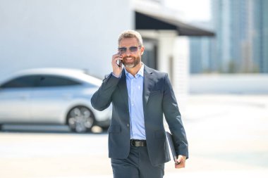 Başarılı bir iş adamı açık havada telefonda konuşuyor. İş adamı dışarıdaki telefonu arıyor. Takım elbiseli olgun iş adamı. Şirket işi. Takım elbiseli zengin iş adamı. Açık hava iş portresi