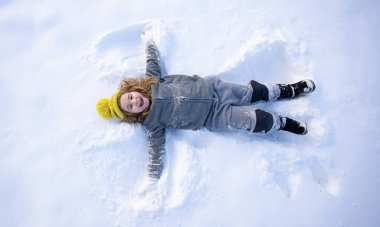Mutlu bir çocuk için eğlenceli bir kış günü. Kar meleği kışın neşeli bir çocuk tarafından yapılmış. Karda uzanmış rahat elbiseli bir çocuk. Tatlı çocuk kar melekleri yapıyor. Kış eğlencesi Neşeli kış anı