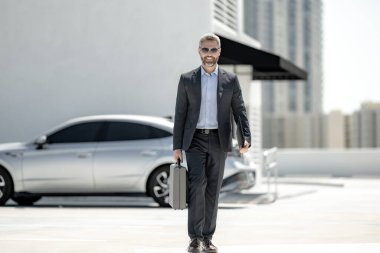 Başarılı bir iş adamı evrak çantasıyla dışarıda dolaşır. İş adamı evrak çantasını dışarıda tutuyor. Takım elbiseli olgun iş adamı. Şirket işi. Takım elbiseli zengin iş adamı. Açık hava iş portresi