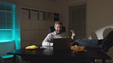 Freelancer gece geç saatlere kadar aperatiflerle çalışıyor. Ofiste atıştırmalık molası. Yorgun çalışanlar için atıştırma molası. Adam ofiste patates kızartması ve pizzayla dinleniyor. Masadaki adam geç saatlerde patlamış mısır yiyor.