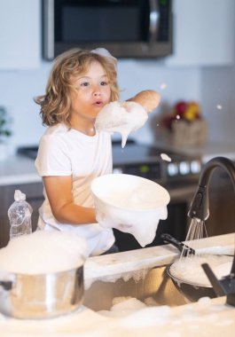 Tatlı çocuk bulaşıkları sabunla yıkıyor. Çocuk bulaşık yıkıyor. Lavaboda bulaşık deterjanıyla çocuk eğlencesi