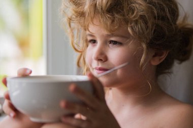 Pencereden bakan rüya gibi bir çocuk. Sakin çocuk, pencereden bak. Çocuk için ev konforu. Çocuğun elinde sabah ışığı olan bir kase var. Konforlu evde çocuk kahvaltısı. Mutlu bir çocukluk. Çocuk pencere kenarında gevşemiş.