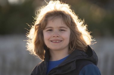 Kameraya bakıp gülümseyen mutlu bir çocuğun portresini yakından çek. Güneş ışığındaki çocuk, açık hava portresi. Çocuk suratlı makro. Mutlu çocuk suratında hayal kur. Çocuk hayalperesti. Yakın çekim çocuk portresi