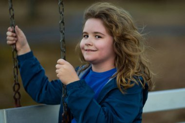 Çocuk dışarıda salıncakta sallanıyor. Dışarıda mutlu bir çocuk var. Çocuk parkında. Özgürlük portresi çocuk. Çocuk dışarıda salıncakta gülümsüyor. Parkta eğlenceli bir çocukluk