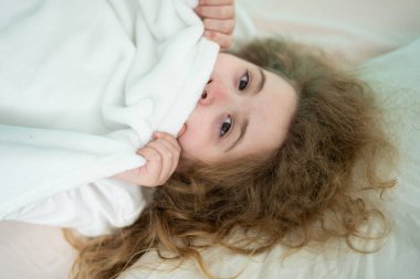 Yüzünün yarısını beyaz bir battaniyenin altına saklayıp kameraya bakan bir çocuk. Şaşkın çocuk yorganın arkasından kötüyü dikizliyor. Çocuk rüyası. Kabustan kork, üstat.