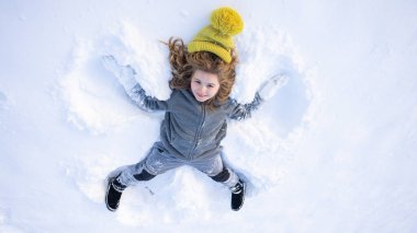 Karda yatan çocuk melek kanatları yapıyor. Melek çocuk kışın oynar. Kar melekleri yapan mutlu bir çocukla kış eğlencesi