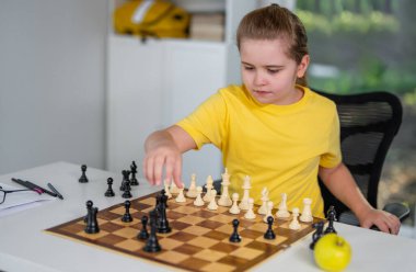 Çocuk satranç düşünüyor. Masada satranç oynayan düşünceli bir çocuk. Akıllı çocuk satrançla mantık öğreniyor. Sınıfta satranç oynayan öğrenciler. Çocuk ve satranç tahtasıyla sıcak bir ev sahnesi