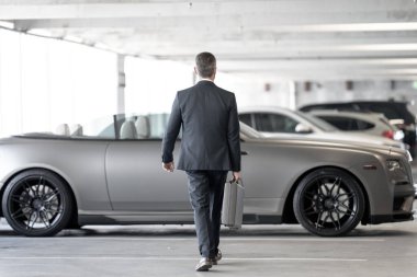 Olgun iş adamı. Zengin iş adamı başarının tadını çıkarıyor. Lüks bir iş. Pahalı arabanın önündeki zengin adam. Lüks iş seyahati. Klasik takım elbiseli, kendinden emin zengin bir iş adamı.