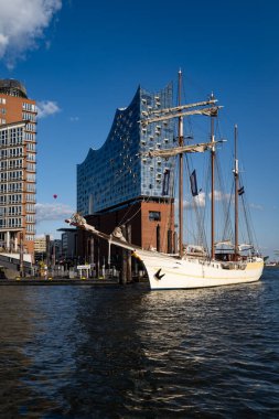 Elbphilharmonie liman mimarisi. Elbphilharmonie binasının liman suyuna yansıması. Elbphilharmonie cam kulesinin önündeki yelkenli. Mimari ahenk. Hamburg 'da Elbphilharmonie