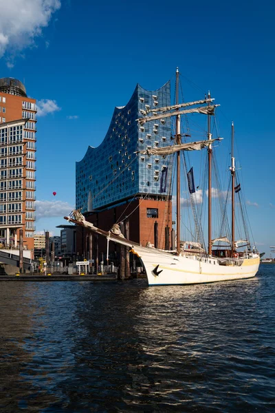Elbphilharmonie liman mimarisi. Elbphilharmonie binasının liman suyuna yansıması. Elbphilharmonie cam kulesinin önündeki yelkenli. Mimari ahenk. Hamburg 'da Elbphilharmonie