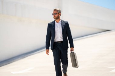 Açık hava iş portresi. Dışarıda yürüyen bir iş adamı. Başarılı lider hareket halinde. Çantalı takım elbiseli adam. İşadamı işe gidiyor. Çantası olan bir iş adamı. İş başarısı