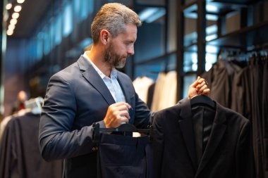 Takım elbiseli, takım elbiseli bir iş adamı. Bir iş adamı mağazada şık bir takım elbise seçer. Modayı takip eden bir müşteri resmi kıyafet alırken ceketi inceler. Klasik kıyafetli çekici bir manken.