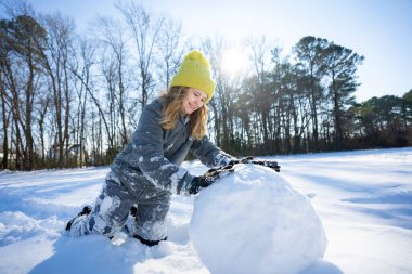 İyi kışlar. Sıcak kış kıyafetleri içindeki çocuk karla oynuyor. Çocuk kış sabahında kar topu yuvarlıyor. Karla oynayan neşeli çocuk. Dışarıda kartopu yapan bir çocuk. Tatlı kız kış havasının tadını çıkarıyor.