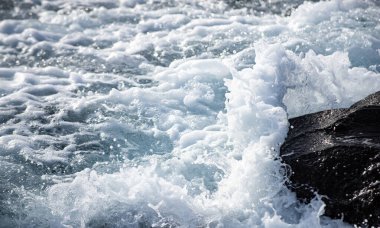 Kayalık kıyı şeridine yakın turkuaz deniz suyu. Su altında taşlarla dolu bir deniz. Mavi dalgalı kıyı manzarası. Okyanus suyu ile tropik deniz kıyısı. Rocky Sahili. Köpük dalgalı mavi deniz yüzeyi