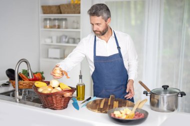 Mutfakta sebze doğruyor. Önlüklü aşçı modern mutfakta sağlıklı yemek hazırlar. Mutfakta sebzeli yemek. Ev mutfağında sebzelerle kahvaltı pişir.