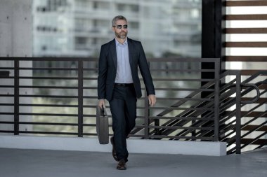 Başarılı bir iş adamı bir evrak çantasıyla dışarıda yürüyor. İş adamı hareket halinde. Takım elbiseli olgun bir avukat. Çantası olan zengin bir iş adamı. Orta yaşlı iş adamı işe gidiyor. Yakışıklı avukat.