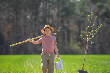 Çocuk kürekle ağaç dikiyor. Çocuk arka bahçeye ağaç dikiyor. Bahar tarlasında çocuk dikme ağacı. Sulama kovası ve kürekle ekmek. Bahçe çiftliğinde ağaç yetiştiren çocuk. Çocuk işi