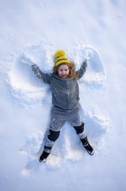 Karda uzanmış rahat elbiseli bir çocuk. Tatlı çocuk kar melekleri yapıyor. Kış eğlencesi Neşeli kış anı