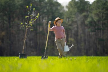 Bahar bahçesi. Çocuk kürekle toprak kazıyor. Bahçesinde ağaç bitkileri olan bir çocuk. Bahçede çalışan çocuklar. Bahçe aletleri. Çocuk bahçıvanlığı. Bahçe işliyorum. Çocuk dikme ağacı. Çiftlikteki çocuk