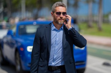 Zengin bir iş adamı pahalı lüks bir arabada. Takım elbiseli zengin bir iş adamı. Şehirdeki başarılı zengin iş adamı. Kendine güvenen bir iş adamı. Başarı işi. İş adamı sokakta yürüyor