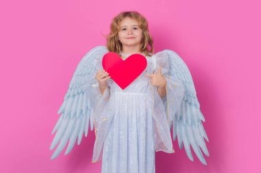 Kalp sembolü aşk ve sevgililer günü olan melek çocuk. Çocuk melek kalbi işaret ediyor, işaret işareti. Sevgililer Günü. Kanatları olan küçük melek çocuk. Meleksi çocuğun stüdyo portresi