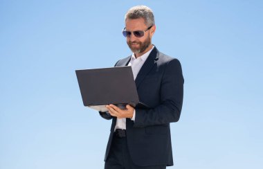 İş adamı dışarıda dizüstü bilgisayar kullanıyor. Dizüstü bilgisayarı olan olgun bir iş adamı. Dizüstü bilgisayarı olan kendine güvenen bir iş adamı. İnternette iş. İş adamı laptoptaki verileri kontrol ediyor. Takım elbiseli iş adamı internette çalışıyor.