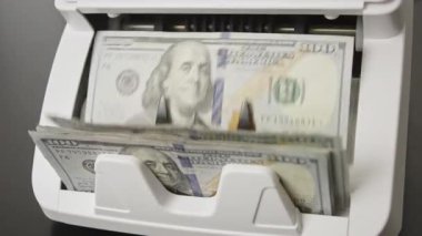 100 dolarlık banknotlar sayım makinesinden geçiyor. İşlem için dolar sayıyorum. Dolar banknotları sayma makinesinde hareket halinde. Kasada Amerikan doları var. Amerikan doları. Dolar banknotları ile yatırım ve tasarruf
