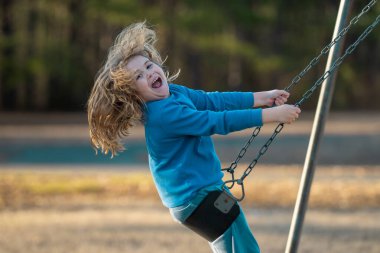 Heyecanlı çocuk eğleniyor. Çocuk bahçesinde mutlu bir çocuk. Havada sallanan tasasız çocuk. Mutlu çocuklar dışarıda oynuyor. Genç çocuk heyecanla sallanıyor. Dışarıdaki oyuncu çocuk. Komik çocuk yüzü.