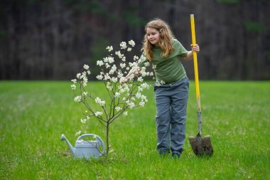 Çocuk dışarıda ağaç dikiyor. Bitkilerin bahar etkinliği. Çocuk kürek ve su bidonuyla çalışıyor. Çocuk meyve ağacı dikmiş. Bahçıvan çocuklar. Çocuk yetiştirme bitkisi ve ağaç bakımı. Bahar tarlasında küçük çiftçi