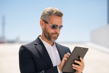 Dışarıda tablet kullanan bir iş adamı. Tabletli başarılı bir iş adamı. Şirket lideri iş adamı tablet üzerinde çalışıyor. Zarif iş adamı tableti kontrol ediyor. İş adamı belgeleri inceliyor