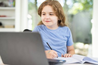 Çocuk evde online çalışmak için dizüstü bilgisayar kullanıyor. Çocuk sanal okul dersinde masada oturuyor. Not defteri ve bilgisayarla öğrenme çağında. Genç bir öğrenci. Çocuklar çevrimiçi uzak sınıf