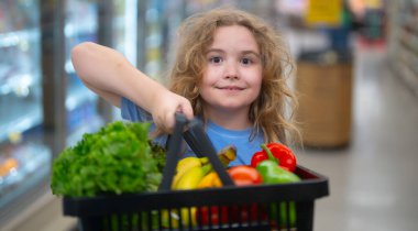 Markette alışveriş arabası olan bir çocuk. Çocuk taze sebze seçiyor. Yakışıklı çocuk sağlıklı yiyecek için alışveriş yapıyor. Süpermarkette yeniyetme. Meyve pazarındaki çocuk. Çocuk marketten sebze alıyor.