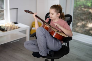 Gitar çalan çocuk. Oturma odasında gitar çalma pratiği yapan bir genç. Çocuk içeride gitar öğreniyor. Müzik dersi sırasında gitarlı bir çocuk. Akustik gitar çalan bir çocuk. Çocuk şarkıları çalışıyor
