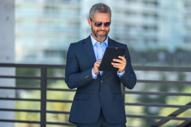 Finans uzmanı bir kontratı inceliyor. Tabletli bir iş adamı. Dışarıda tablet kullanan bir iş adamı. Olgun iş adamı finans verilerini kontrol ediyor. Zengin iş adamı tabletteki sözleşmeyi gözden geçiriyor