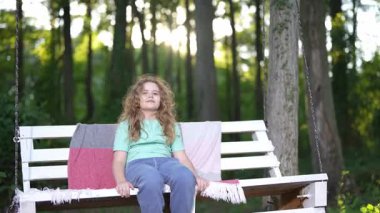 Tahta salıncakta rahat bir çocuk. Bahçe salıncağında dinlenin. Çocuk dışarıda rahatça oturuyor. Çocuk huzurlu bir doğada. Çocuk temiz havanın tadını çıkarıyor. Çocuk orman sahnesinde dinleniyor. Çocuk bankta dinleniyor.