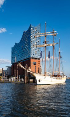 Elbphilharmonie liman mimarisi. Elbphilharmonie binasının liman suyuna yansıması. Elbphilharmonie cam kulesinin önündeki yelkenli. Mimari ahenk. Hamburg 'da Elbphilharmonie