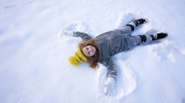 Mutlu çocuk kış günü kar meleği yapıyor. Dışarıda karda yatan gülümseyen çocuk. Çocuk soğuk kış havasının tadını çıkarıyor. Dışarıda karda oynayan neşeli bir çocuk. Çocuk karda eğleniyor.