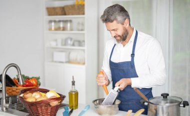 Taze sebze pişiren bir şef. Ev yapımı yemek pişiren bir adam. Mutfakta sağlıklı bir kahvaltı için sebze pişiren bir aşçı. Üniformalı aşçı modern bir mutfakta sebze pişiriyor.