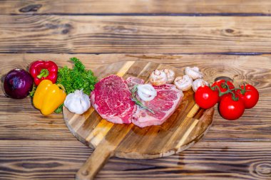 Raw beef steak on wooden board with ingredients. Fresh sliced meat prepared for cooking. Beef fillet with rosemary and pepper. Raw beefsteak. Fresh meat slice ready for grill or barbecue