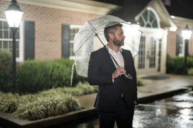 İş adamı gece yağmurda yürür. Bir iş adamı yağmur altında kendine güveni ve tarzıyla durur. Yağmurlu bir gecede bekleyen sabırlı bir adamın portresi. Gece yağan yağmurda işadamı