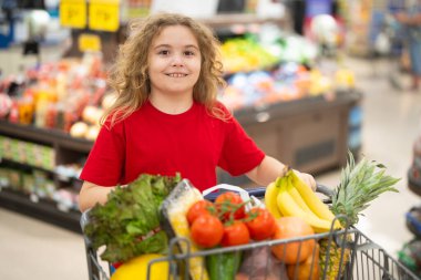 Markette alışveriş arabasıyla çocuk alışverişi. Çocuk markette taze sebze seçiyor. Markette yiyecek alışverişi yapan çocuk. Yerel bir dükkanda sağlıklı ürünler seçen bir çocuk. Bakkalda taze yiyeceği olan çocuk.