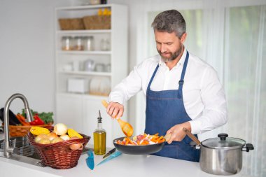 Mutfakta sebze pişirmek. Önlüklü şef, çiğ malzemeyle sağlıklı bir yemek hazırlar. Sebzeli yemek. Akşam yemeği için taze sebzelerle yemek pişir. Aşçı sebzelerle kahvaltı hazırlar.