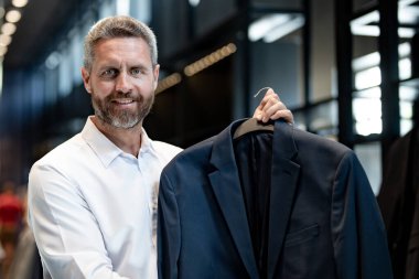 Bir adam butikte alışveriş yaparken klasik bir terzi kıyafeti giyer. Başarılı bir iş adamı için klasik bir kıyafet. Takım elbiseli modaya uygun bir mağaza. Takım elbise seçen bir iş adamı. Bir erkek resmi etkinlik için takım elbise seçer.